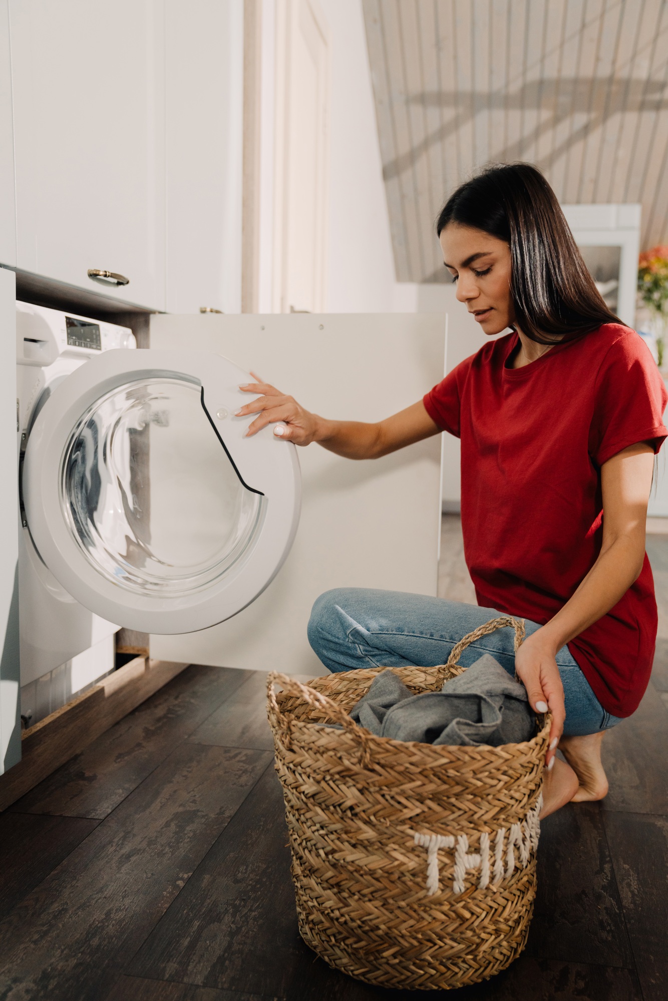Young woman putting clothes at washing machine while doing laundry